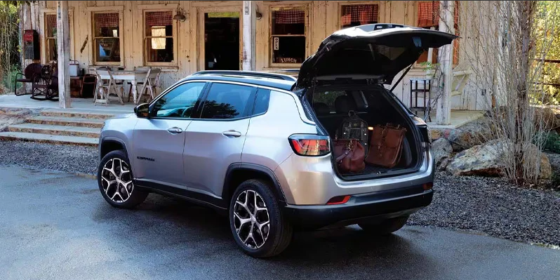A photo of a 2025 Jeep Compass parked in a driveway with the trunk open with bags in the back.