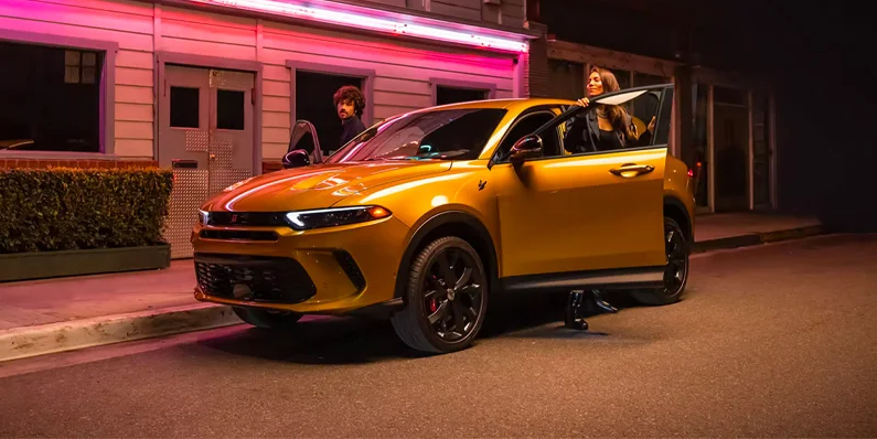 A photo of a yellow 2025 Dodge Hornet parked on the side of the road with a woman climbing in to the drivers side.