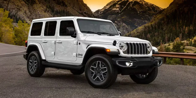A 2025 Jeep Wrangler parked on the side of the road with a sunset in the background.