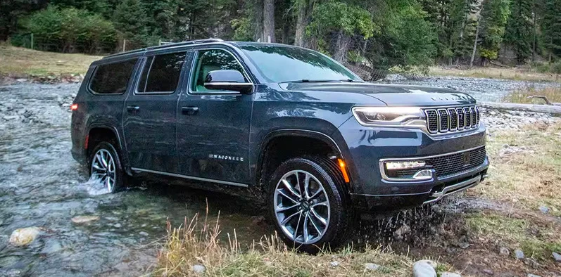 A dark blue 2025 Jeep Wagoneer off-roading through a stream of water.