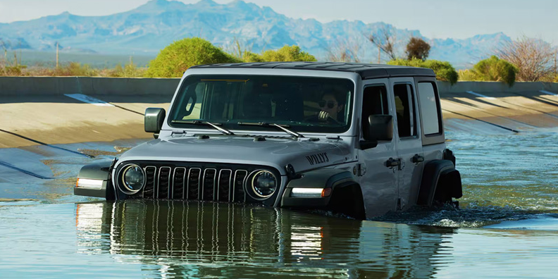 A grey 2026 Jeep Wrangler driving through water.