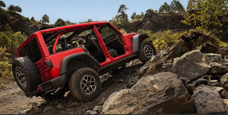 A red 2026 Jeep Wrangler off-roading up a rocky hill.